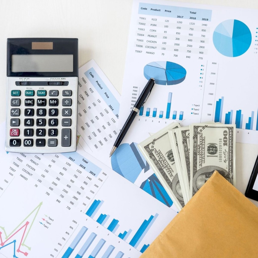 Financial planning desk with project cost reports, budget charts, calculator, and business analysis documents for contractors and project-based businesses